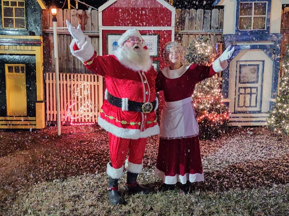 an image of Santa Clause and Mrs. Clause in front of a festive Christmas home