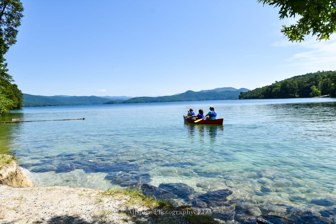 a clear blue lake with a mountain view in the background and three people rowing a canoe in the water.